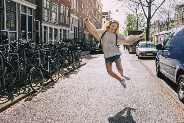 Junge Frau im Pullover und Minirock, die auf einer Straße fröhlich in die Luft springt