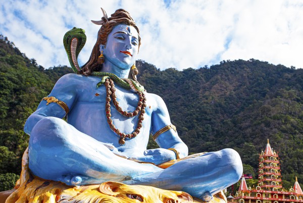 Blaue Shiva Statue mit grünen Bergen im Hintergrund in Rishikesh am Ganges