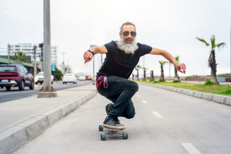 Strahlender, sportlicher Senior-Skater mit Bart und Sonnenbrille in voller Fahrt auf dem Board